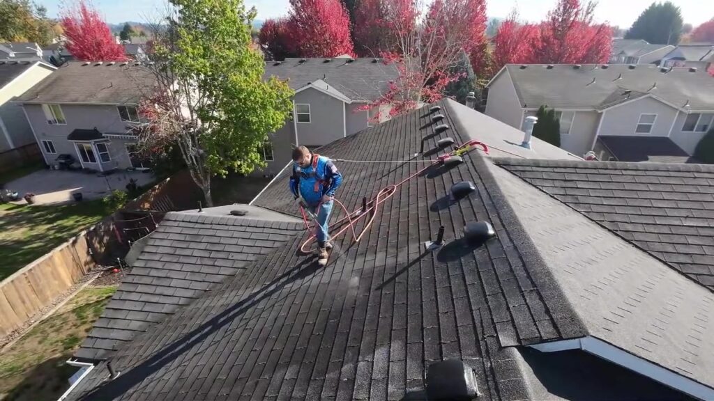 Mountain View technician in a safety harness soft washing an asphalt shingle roof, seen from a drone