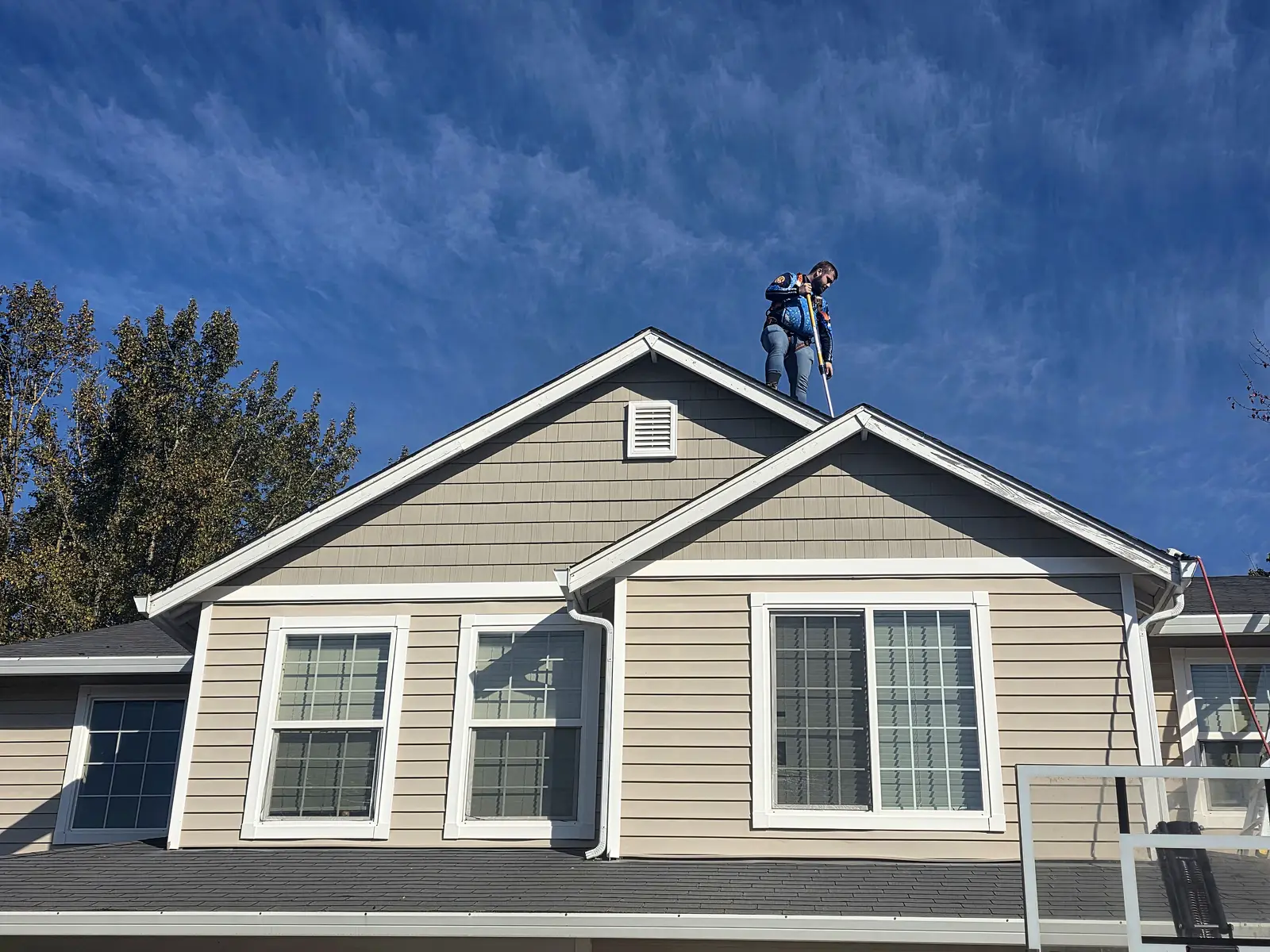 Technician from Mountain View Pressure Washing And Softwash on the roof of a two-story home during roof cleaning